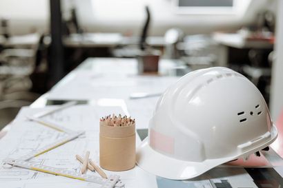 White hard hat on an architect’s desk with pencils, rulers, and blueprints in the background