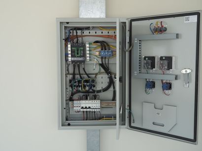 Open electrical control panel cabinet with wiring, breakers, and mounted components exposed