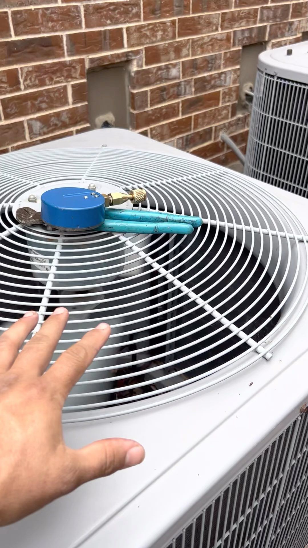 A person is holding a pair of pliers on top of an air conditioner.