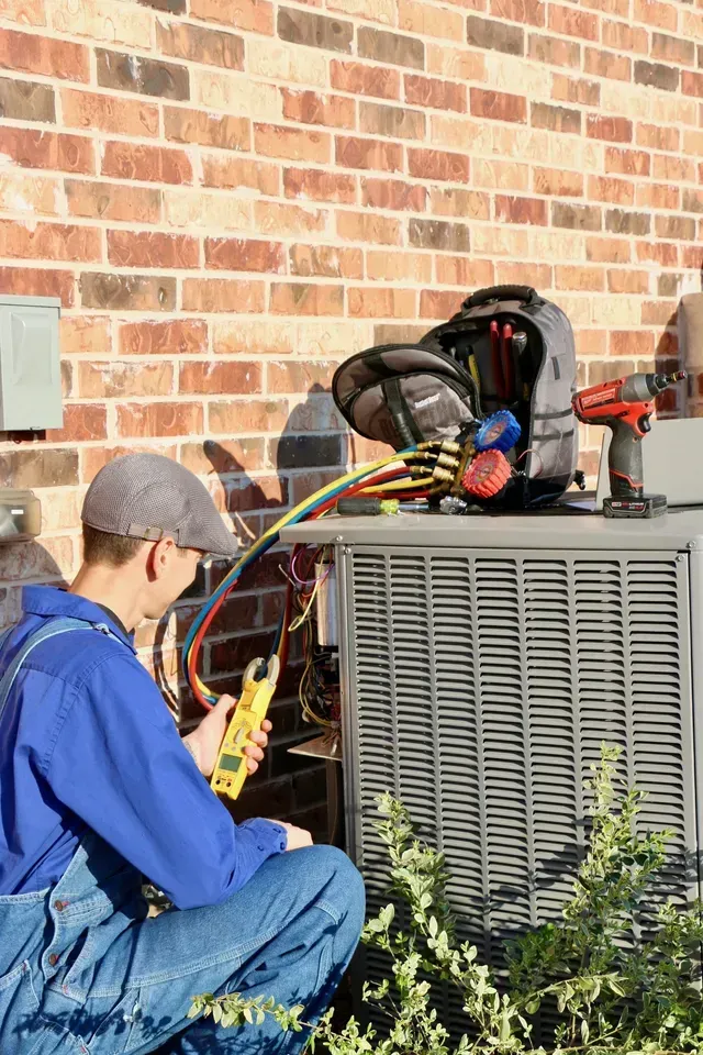 A man is working on an air conditioner outside of a brick building.