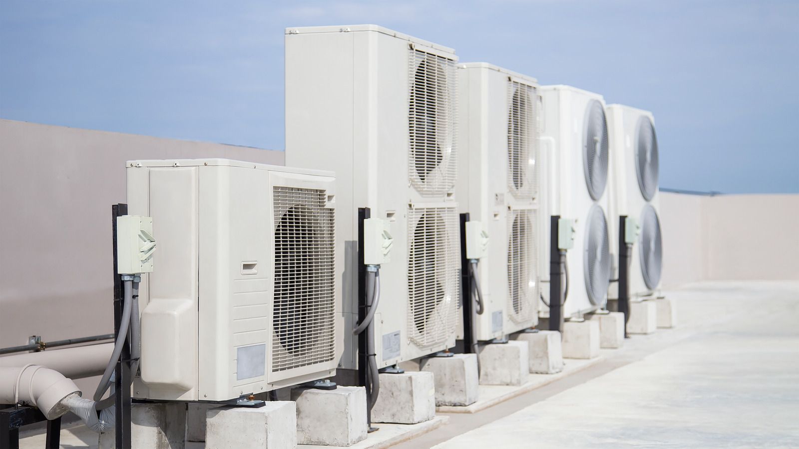 Row of white air conditioning units on a rooftop against a blue sky.