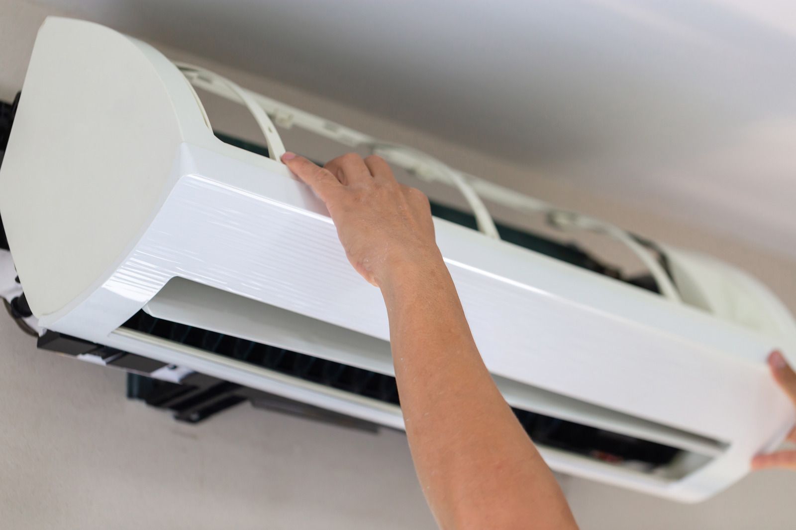 A person is cleaning an air conditioner from the ceiling.