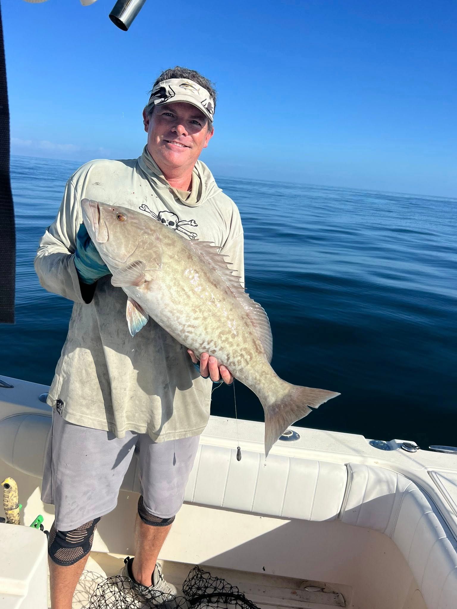 Man on a boat holding a large fish he caught, blue sky, sunny day.