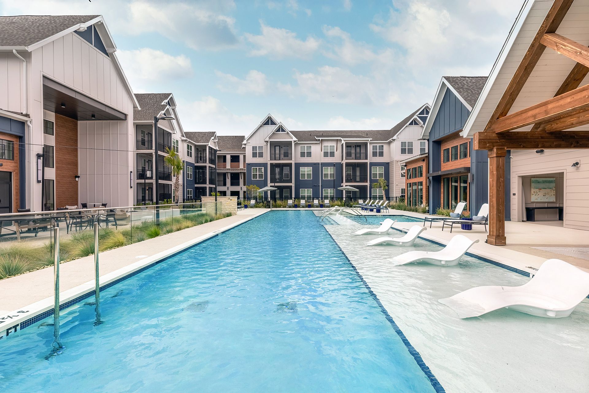 Modern apartment complex pool with lounge chairs and blue water under a cloudy sky