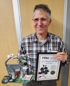 A man in a plaid shirt is holding a pvma certificate
