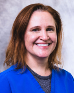 A woman in a blue scrub top is smiling for the camera.