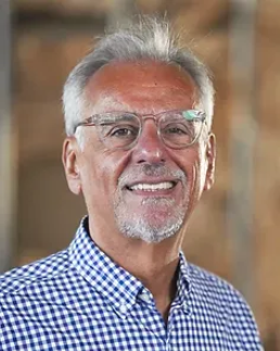 A man in a white coat and tie is smiling for the camera.