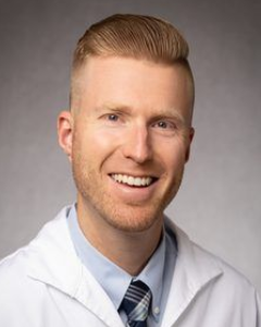 A man in a white coat and tie is smiling for the camera.