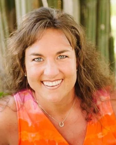A woman in an orange shirt and necklace is smiling for the camera.