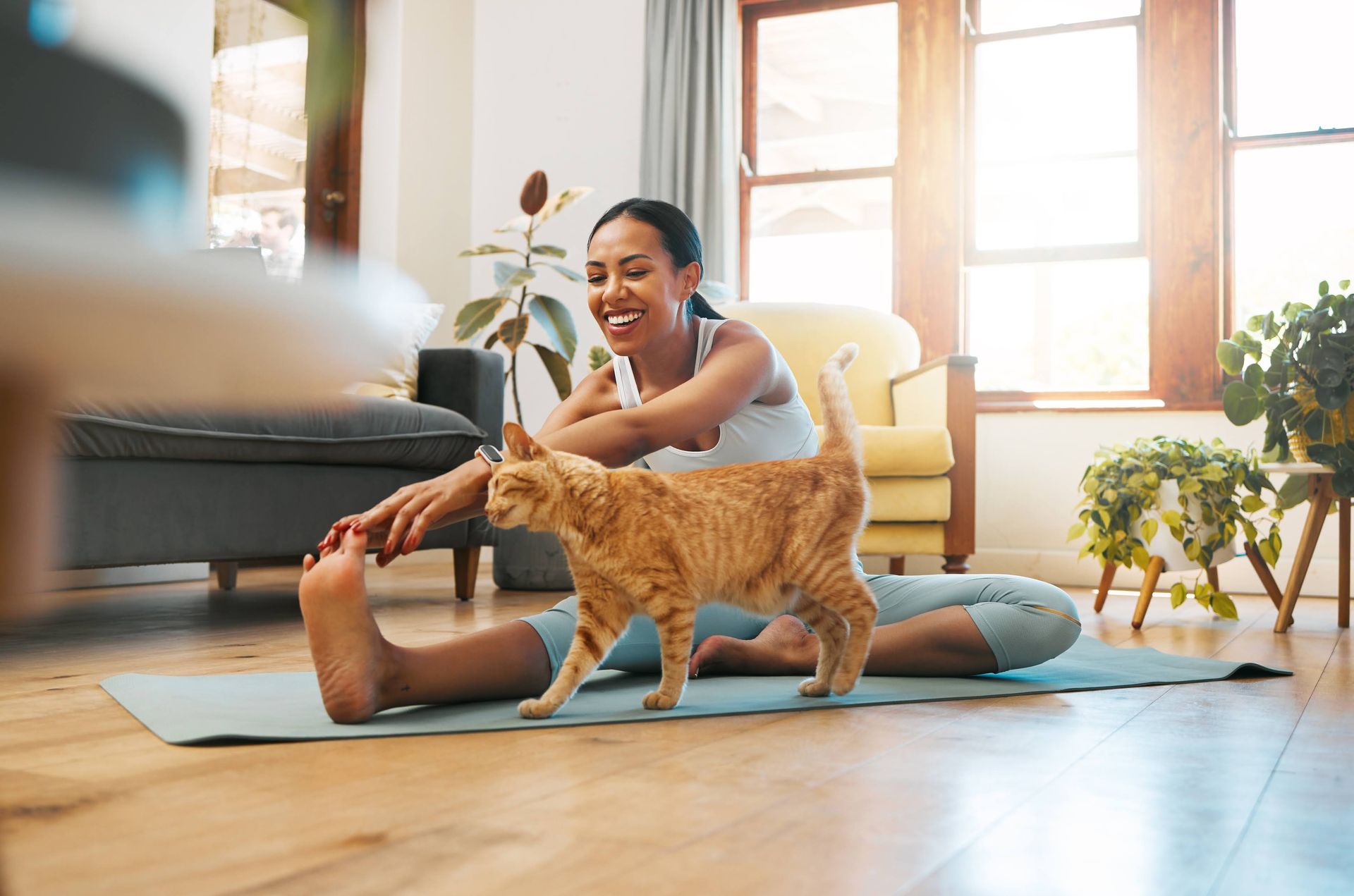 A woman is stretching on a yoga mat with her cat.