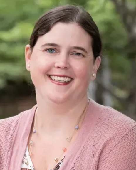 A woman in a pink sweater and necklace is smiling for the camera.