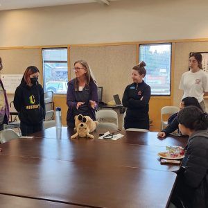A group of people are standing around a table with stuffed animals on it.
