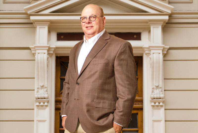 Man in a brown blazer standing in front of an ornate white building facade