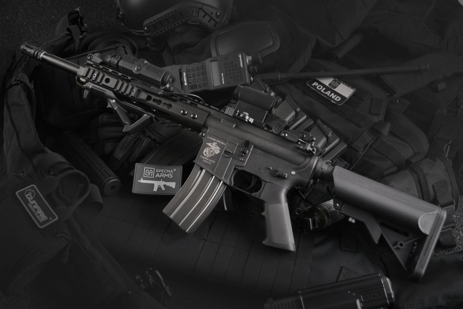 Black tactical rifle with scope and magazines laid on a dark background.