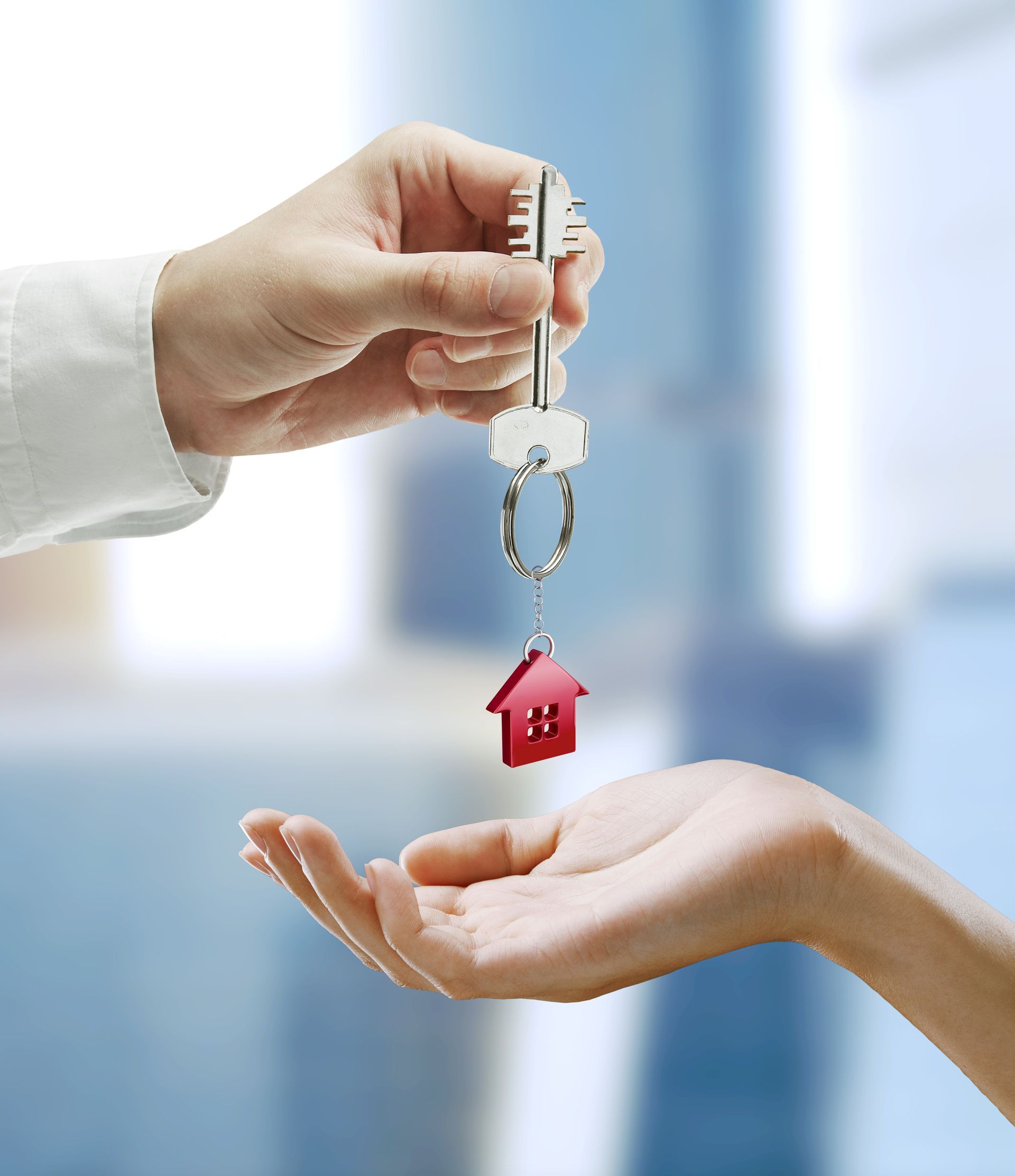Handing over a house key between two hands, with a red house keychain.