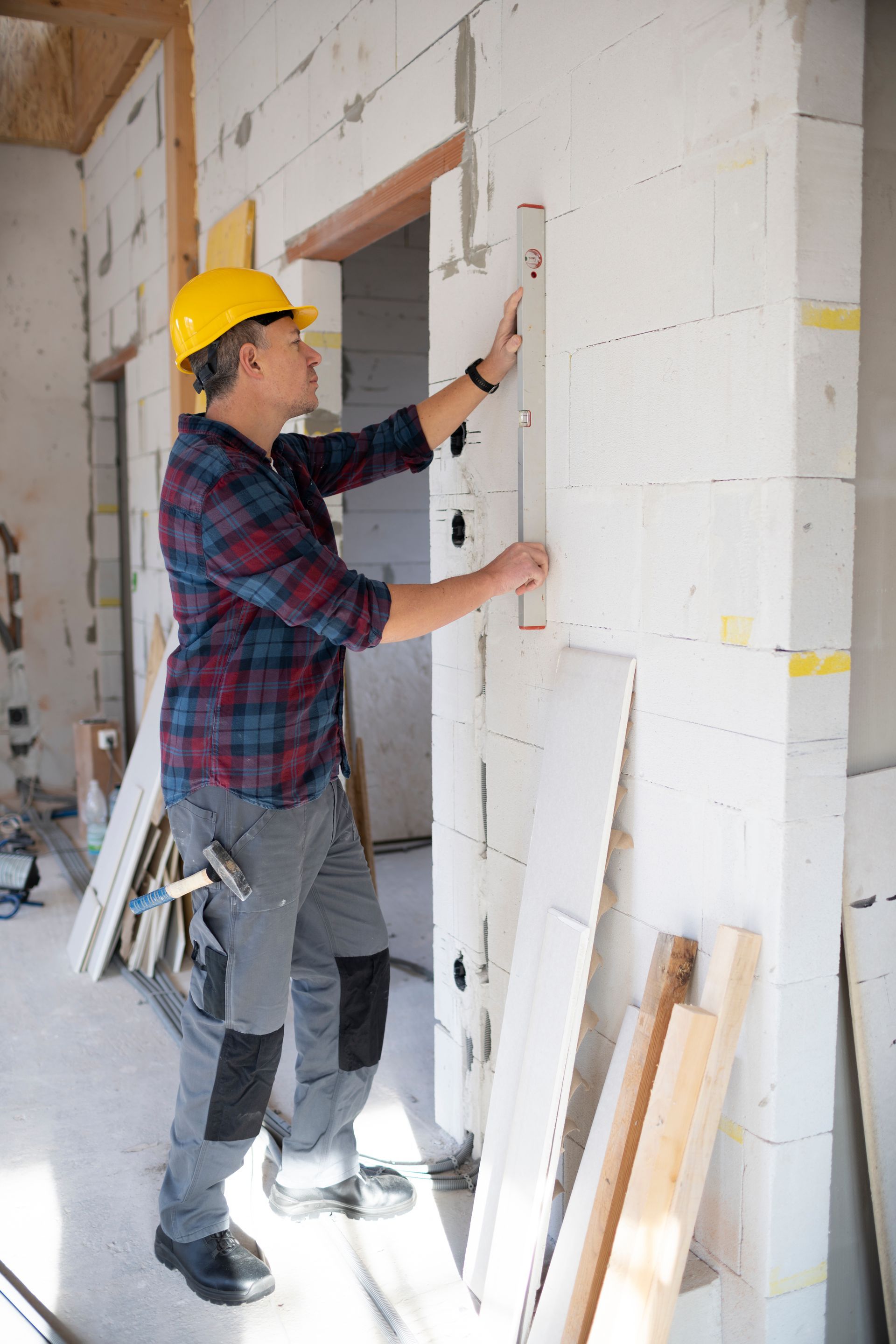 Worker in a yellow hard hat measuring a doorway in an unfinished room with white walls.