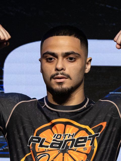 Man holding both arms up, wearing a black shirt with orange “10th Planet” logo