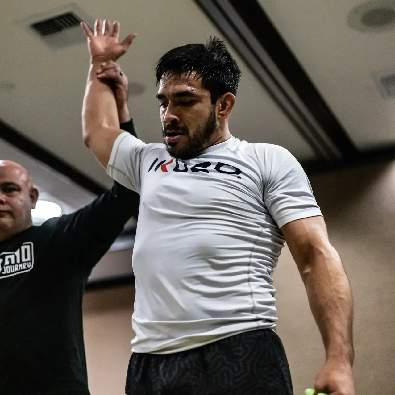 Athlete in white shirt raises one arm during a training session indoors