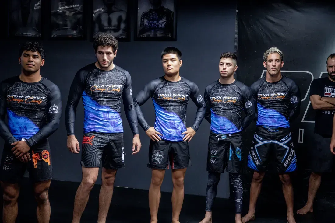 Six athletes in matching blue-and-black uniforms stand on a dimly lit stage before a competition.