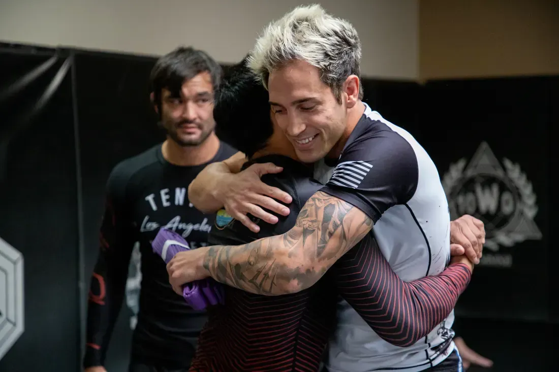 Two men in athletic gear embrace after a training session in a gym.