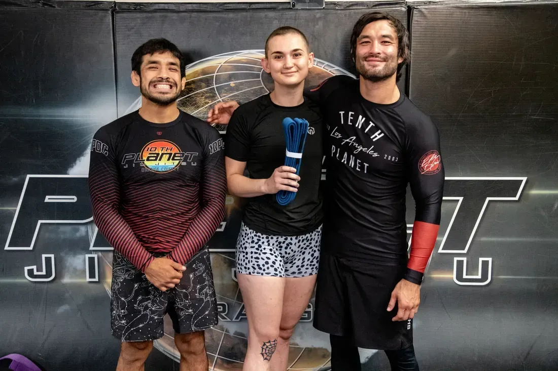 Three people posing in front of a gym wall, one holding a blue trophy.