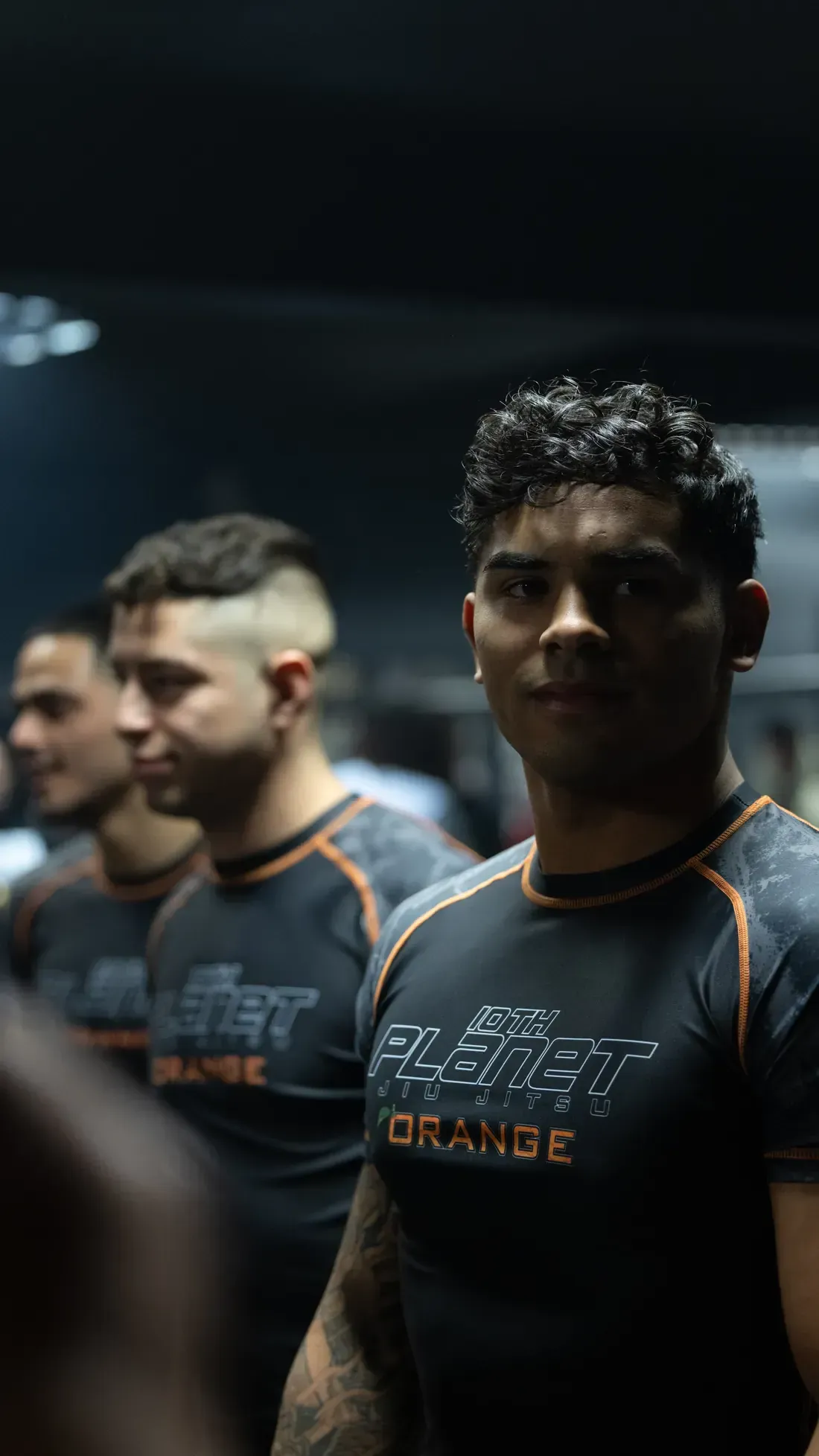 Athletes in dark jerseys with orange trim standing in a dimly lit gym or arena.