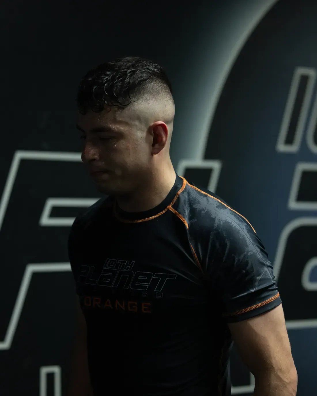 Athlete in a black and orange shirt standing against a dark gym wall