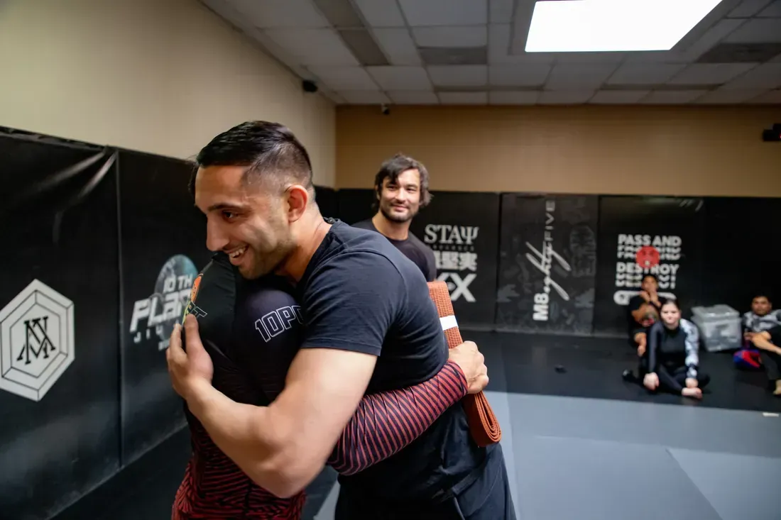 Two people practicing a grappling hold in a martial arts gym with mats and wall pads
