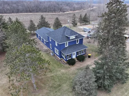 Blue two-story house with dark roof and white trim surrounded by trees in a rural setting.