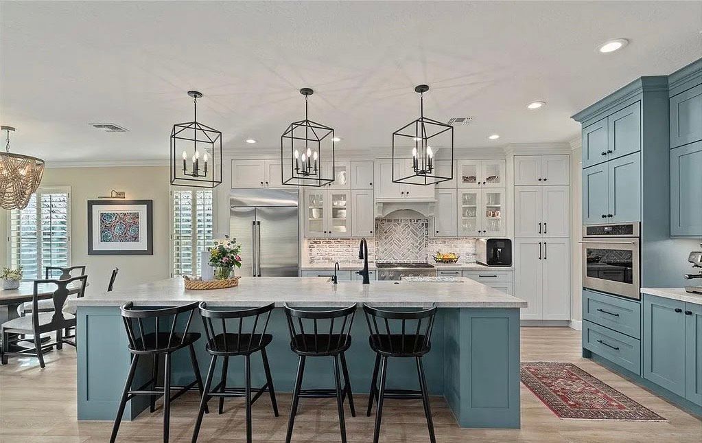 Spacious kitchen with blue and white cabinets, large island with black stools, and pendant lights.