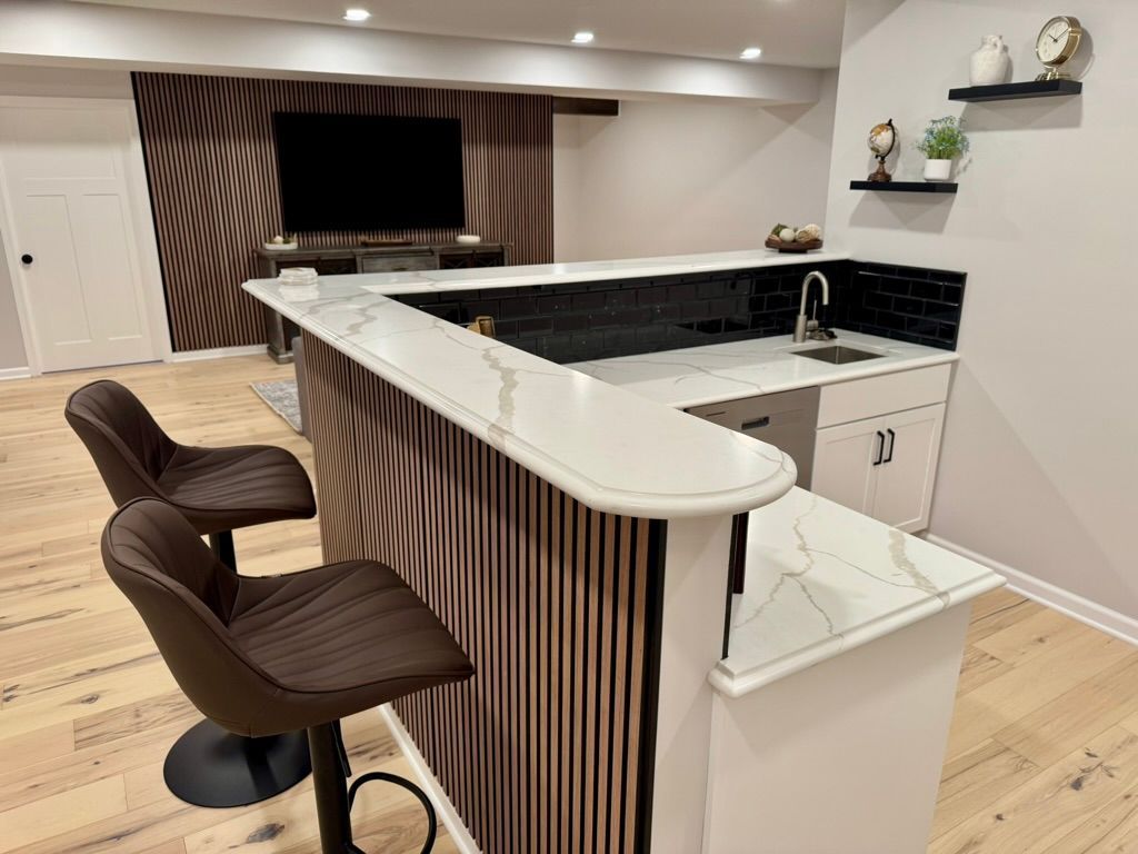 Basement bar with brown and white counter, two bar stools, TV, and decorative wall.