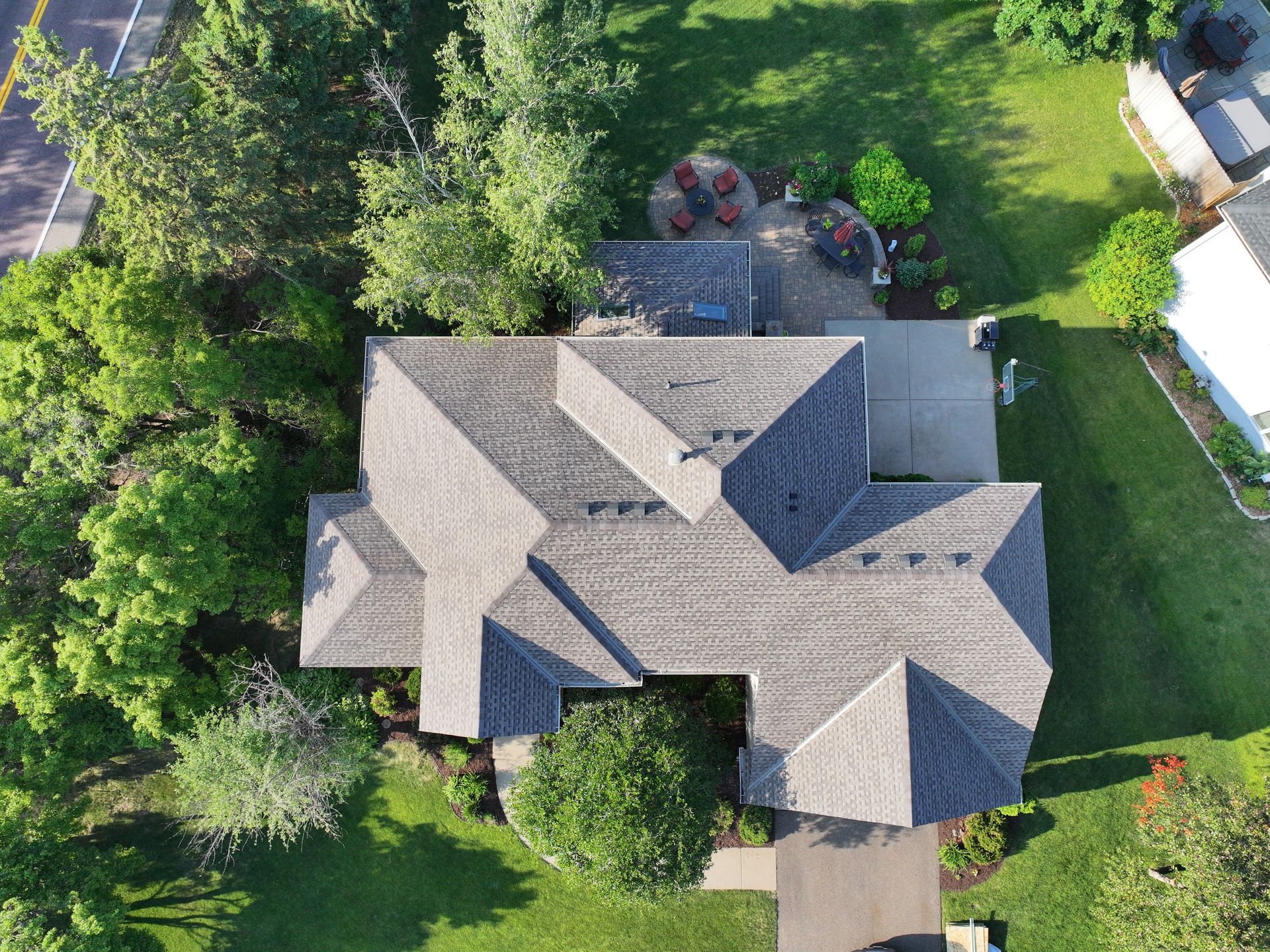 Overhead view of a house with a gray roof surrounded by trees and a green lawn.