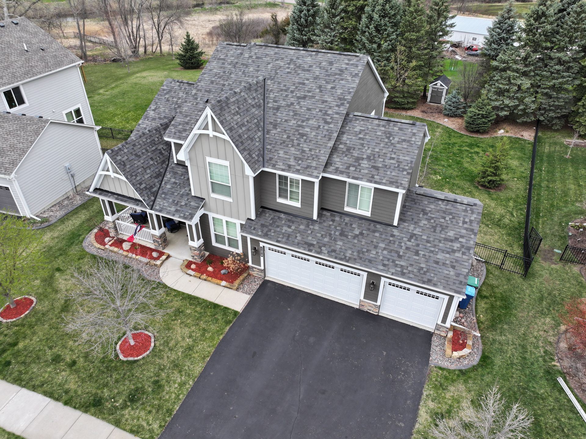 Aerial view of a gray two-story house with a dark driveway and a well-manicured lawn.