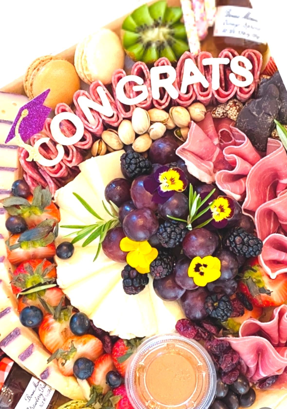 Charcuterie board with "CONGRATS" message, cheese, fruit, nuts, and meats, celebrating graduation.