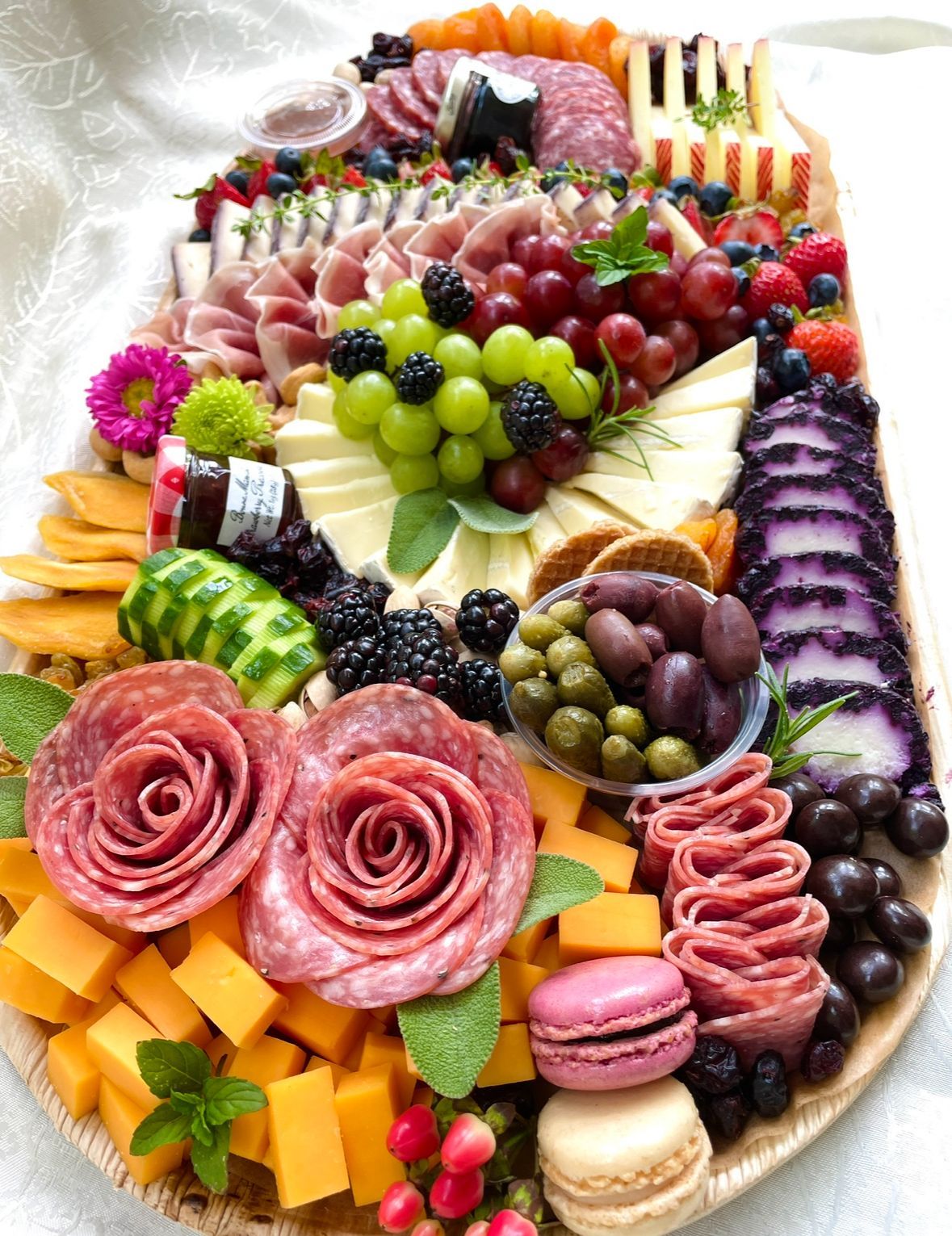 Charcuterie board with salami roses, cheeses, fruits, olives, and macarons.