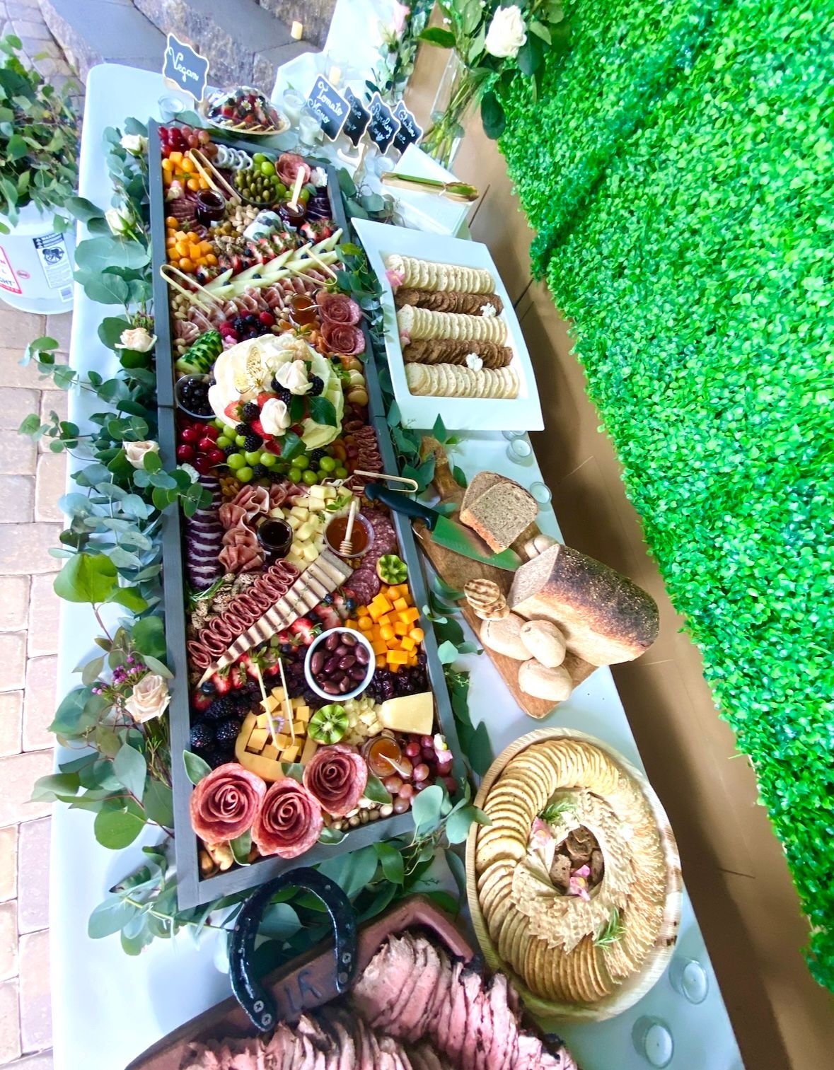 Charcuterie spread on a table with crackers, cheese, grapes, and meats, decorated with greenery and flowers.