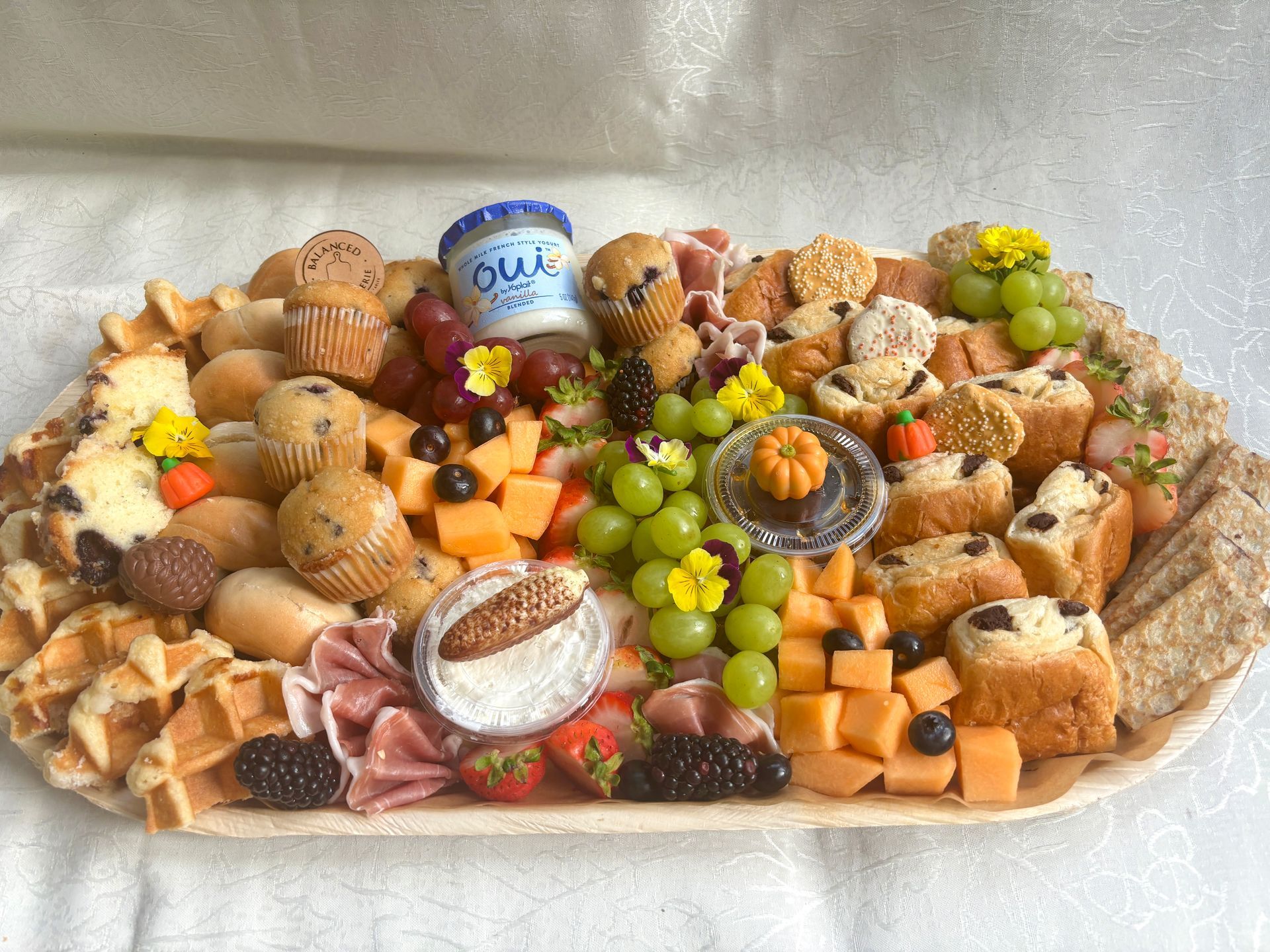 Charcuterie brunch board with various breakfast items like muffins, waffles, fruits, and yogurt.