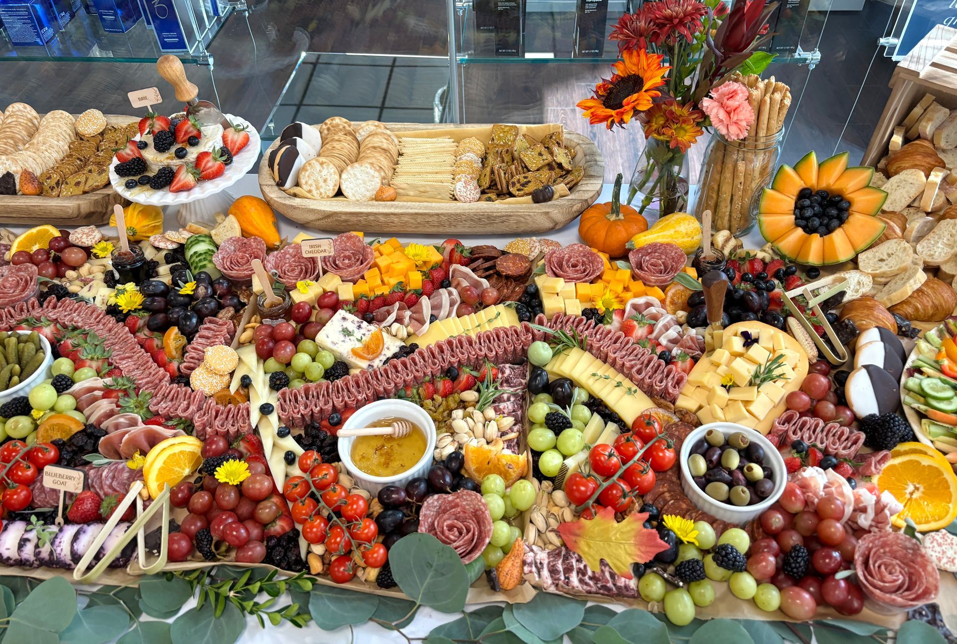 Charcuterie board with cheeses, meats, crackers, grapes, and other snacks. Decorated with fall foliage.