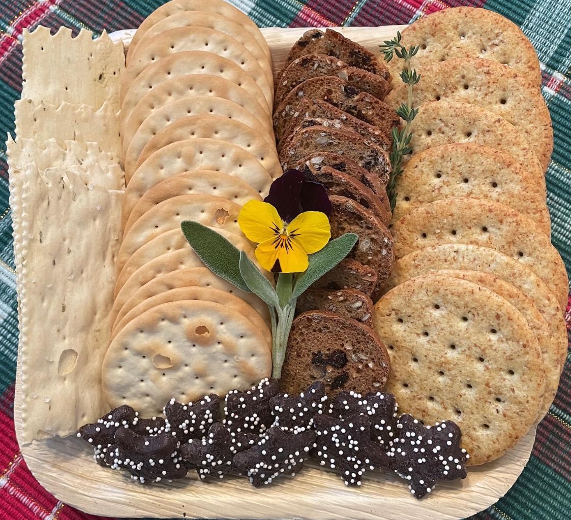 Cracker assortment on a wooden platter with a floral garnish, arranged on a plaid surface.