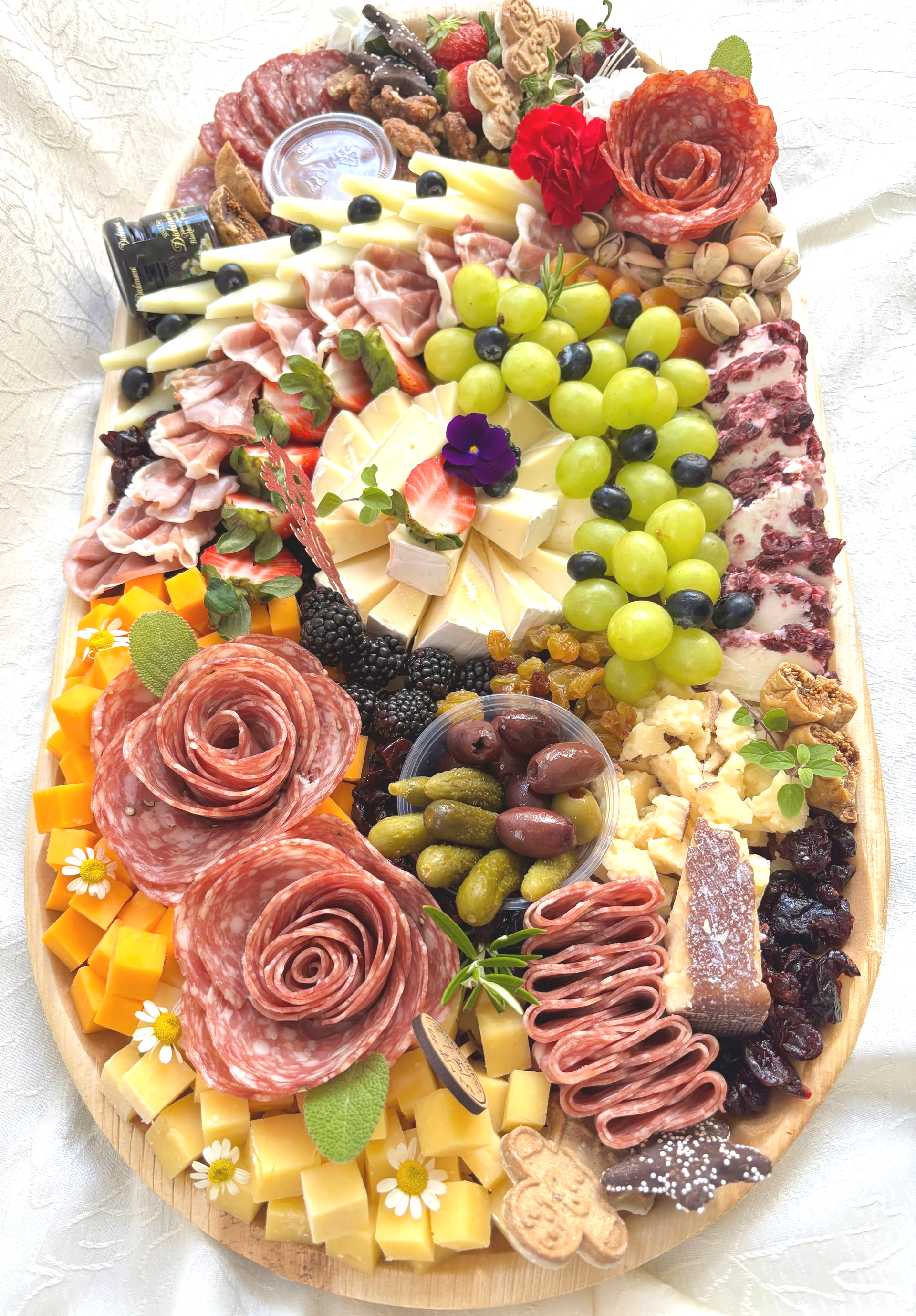 Oval charcuterie board with cheese, meats, fruits, nuts, and 