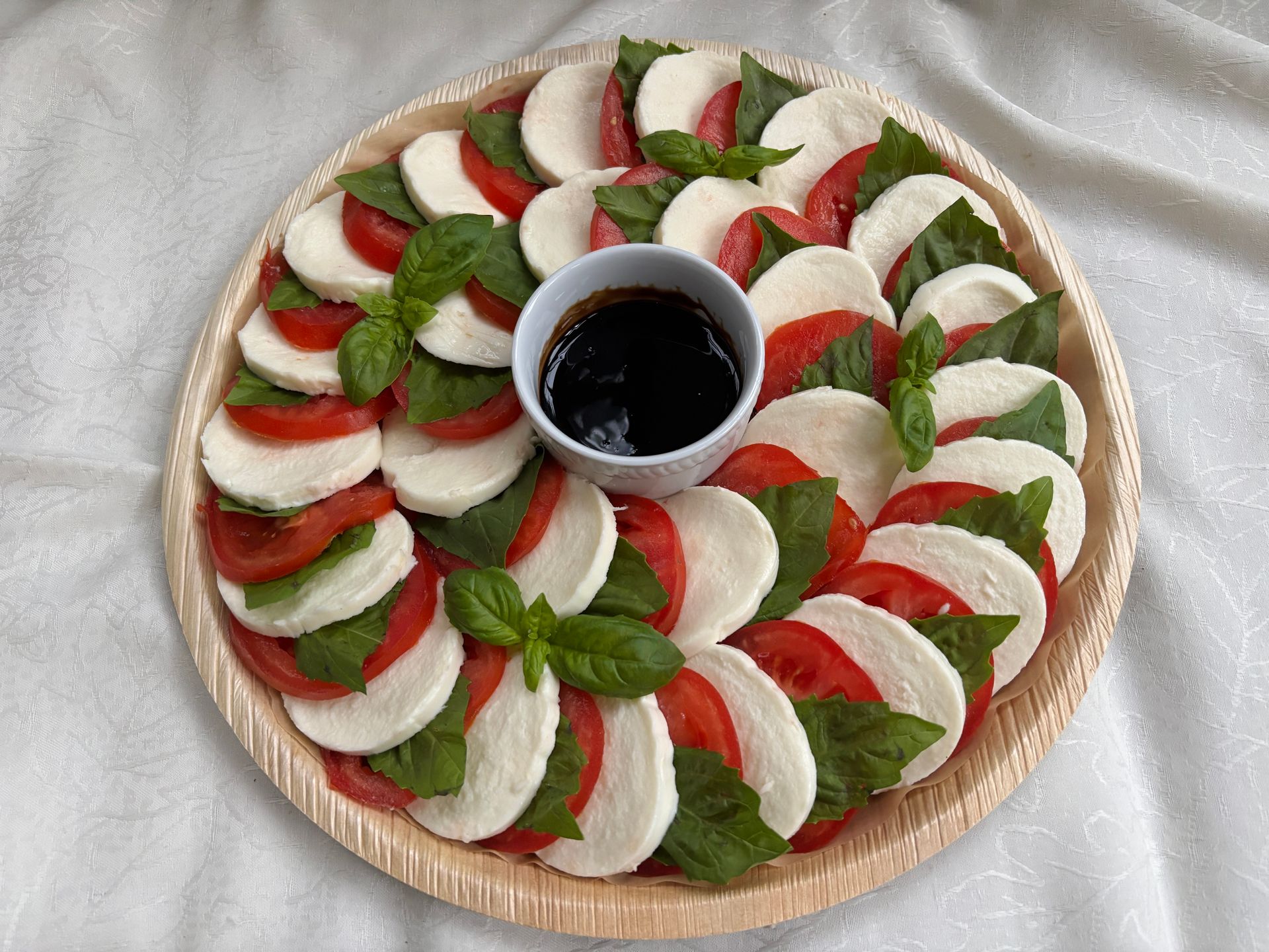 Caprese salad on a wooden platter: tomato, mozzarella, basil arranged with balsamic glaze.