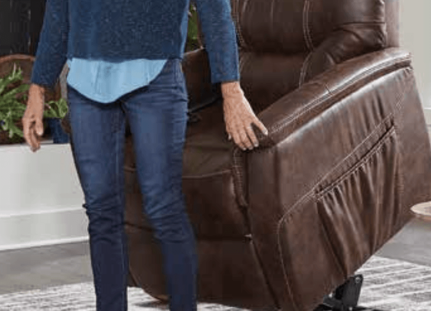 A woman is standing next to a brown recliner in a living room.