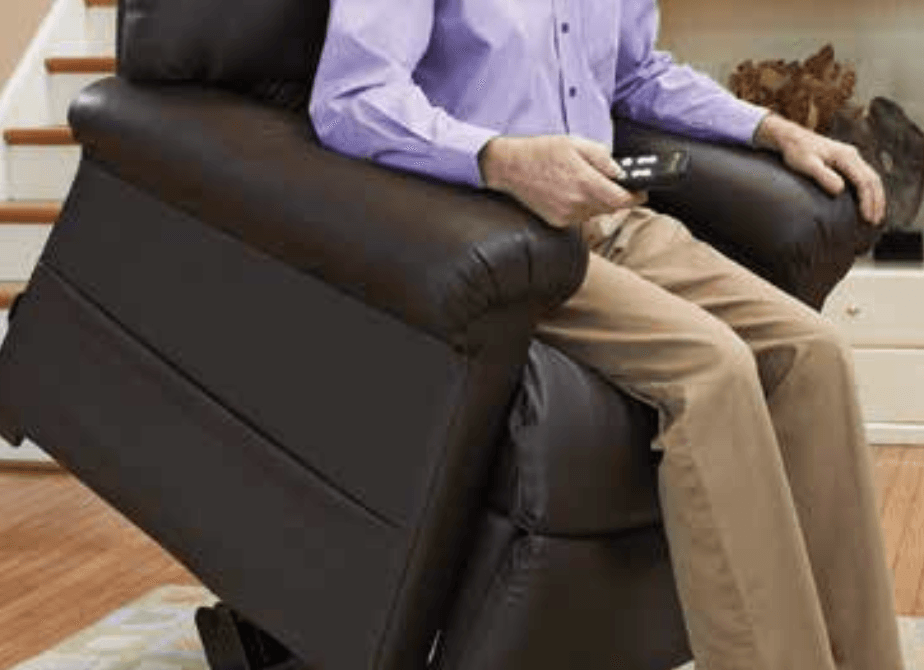 A man in a purple shirt is sitting in a recliner holding a remote control.