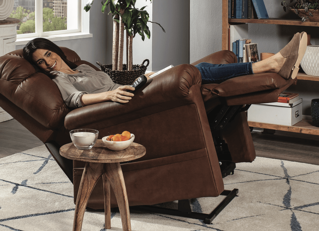A woman is laying in a brown leather recliner in a living room.