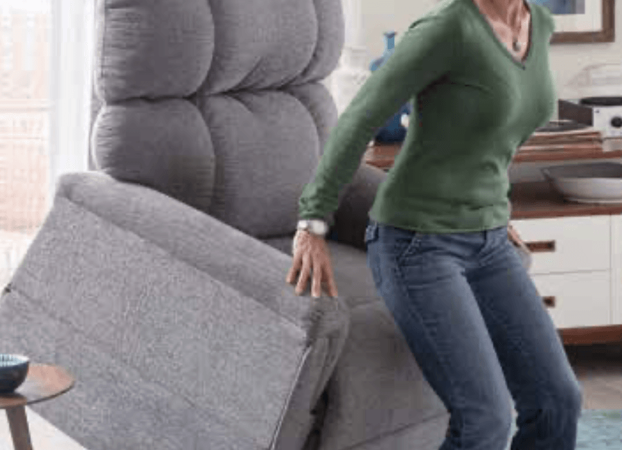 A woman is standing next to a recliner in a living room.