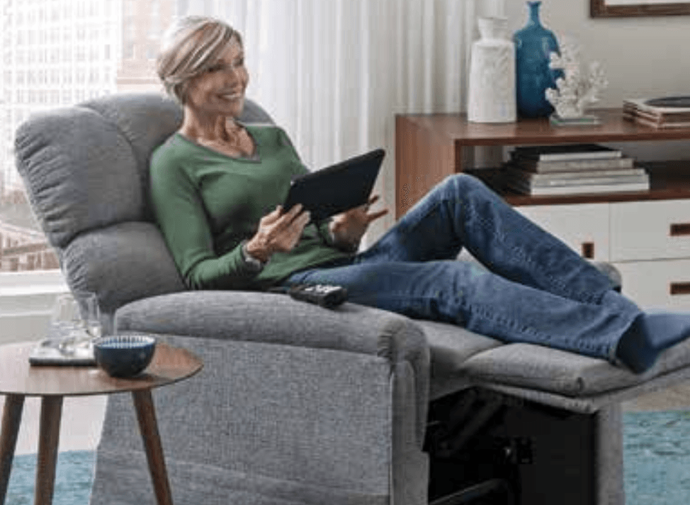 A woman is sitting in a recliner using a tablet computer.
