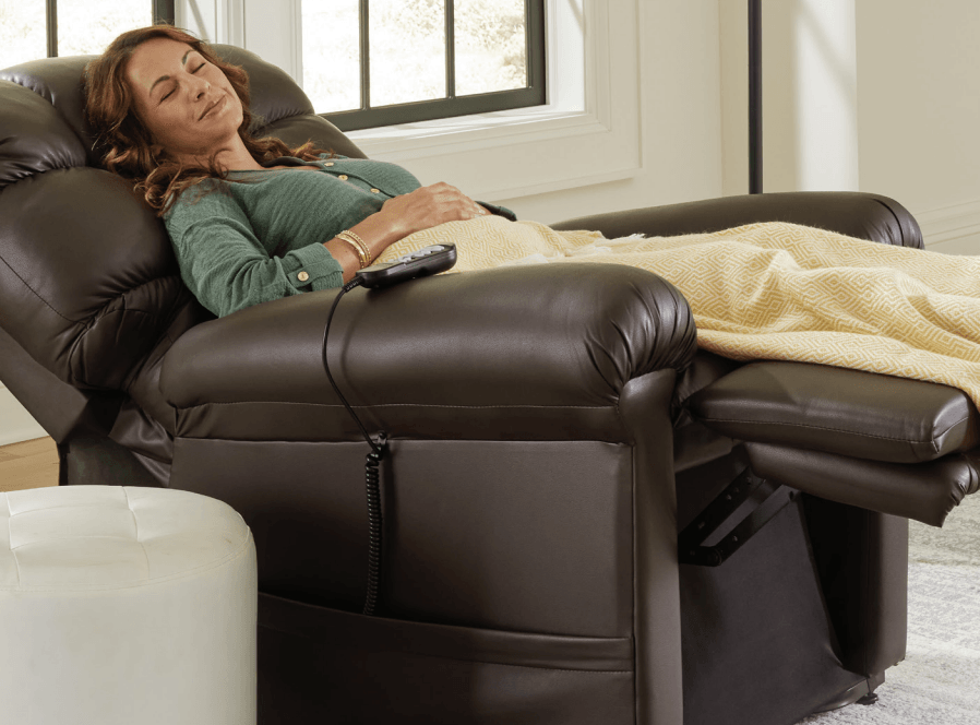 A woman is laying in a recliner with a remote control.