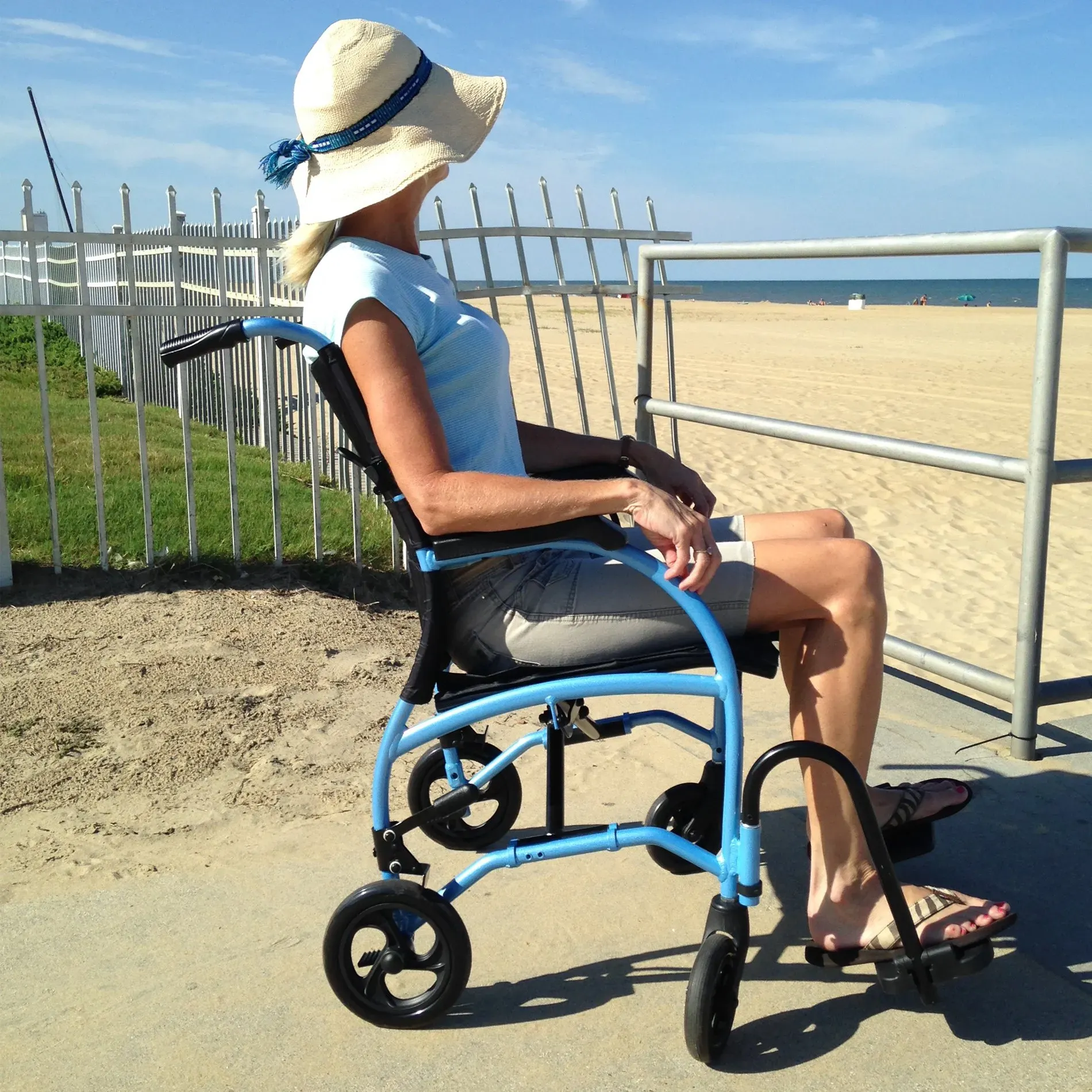 A woman wearing a hat sits in a wheelchair on the beach