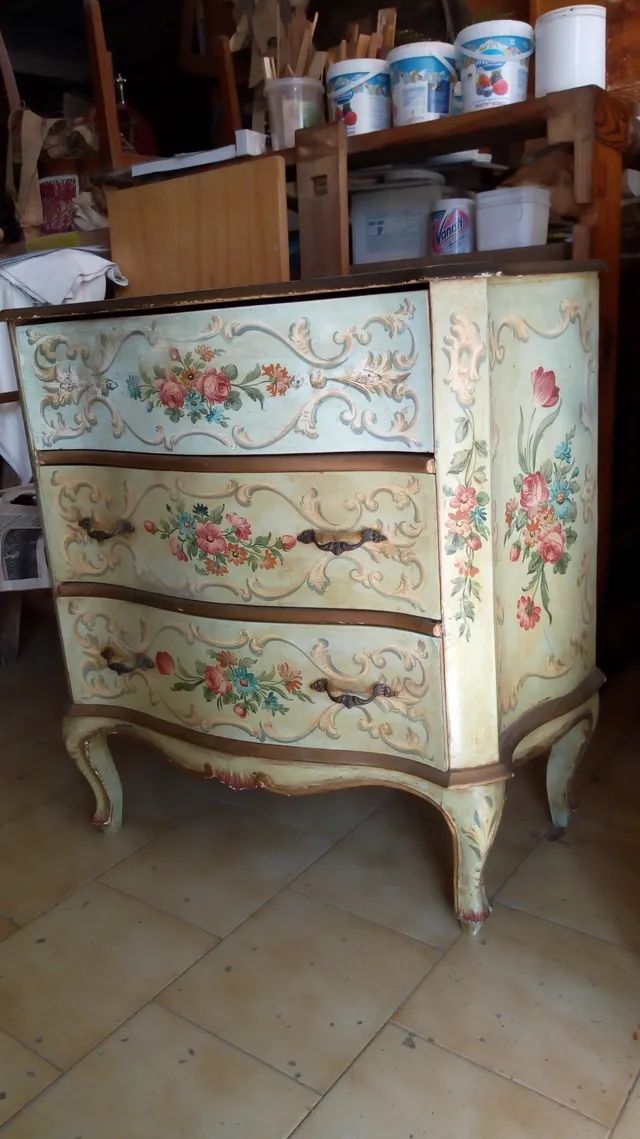 Una cassettiera con dei fiori dipinti è appoggiata su un pavimento piastrellato.