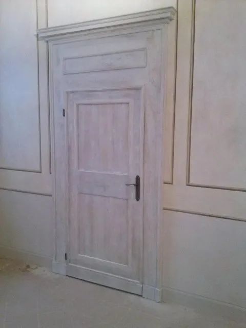 Una porta bianca con una maniglia nera si trova in una stanza con le pareti bianche.